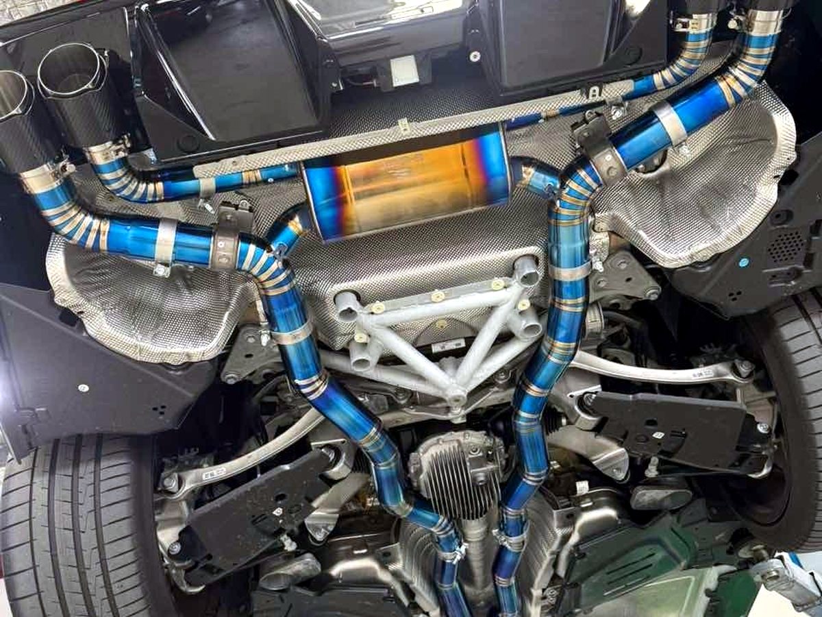 BMW M5 G90 underbody with OUCHI titanium valved mid-rear exhaust, heat-tinted blue — customer installation