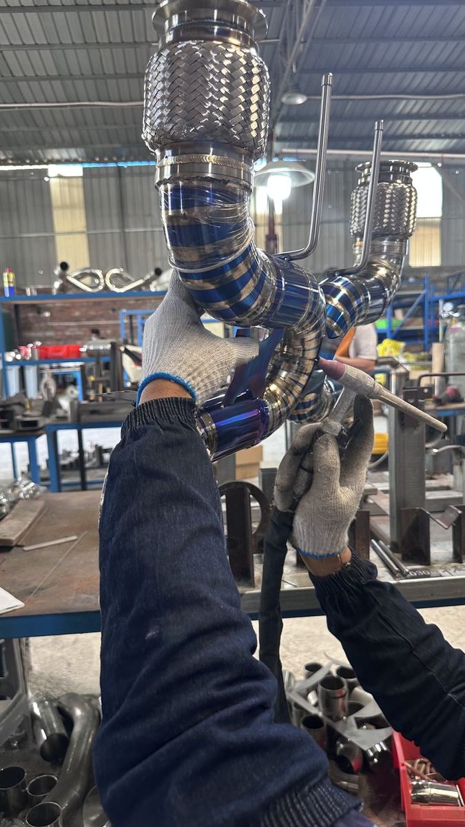 Welder fitting a heat-tinted GR5 titanium exhaust assembly